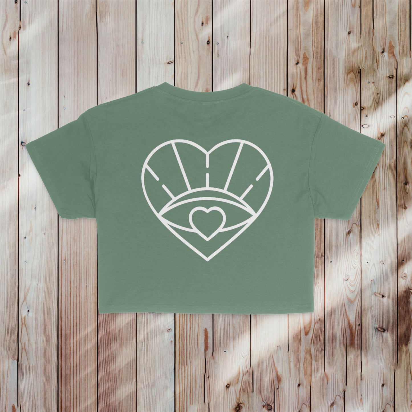 A stylish smoky sage crop tee with a white heart and evil eye design, representing the Moms Have More Fun brand. Ideal for adding flair to your mom wardrobe